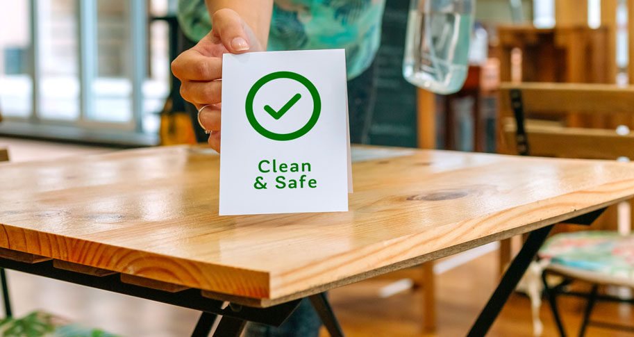 A "Clean & Safe" sign with a checkmark being set on a table. 