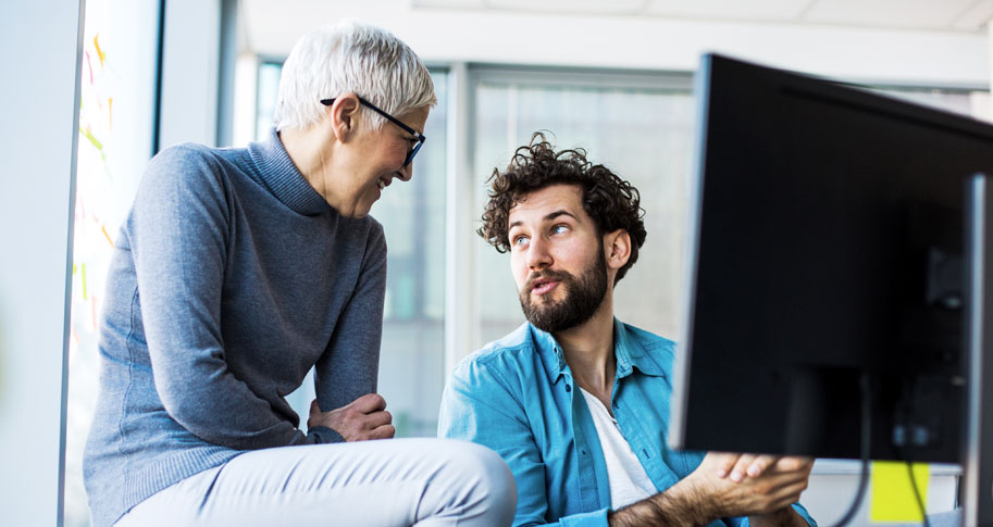 Young male helping older female coworker work on computer