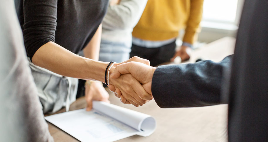 Cropped shot of businessman greeting a young professional around the table in office. Close up of business people shaking hands in office.