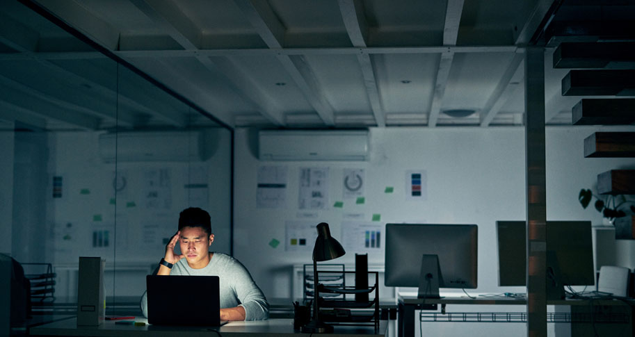 Man that looks stressed, in a dark room working on his laptop