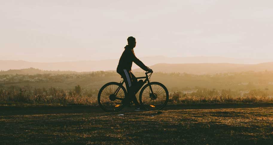 A man biking with hills behind him