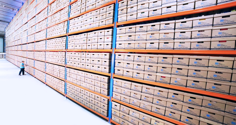 A man stands in front of tall racks of boxes of inventory in a warehouse.