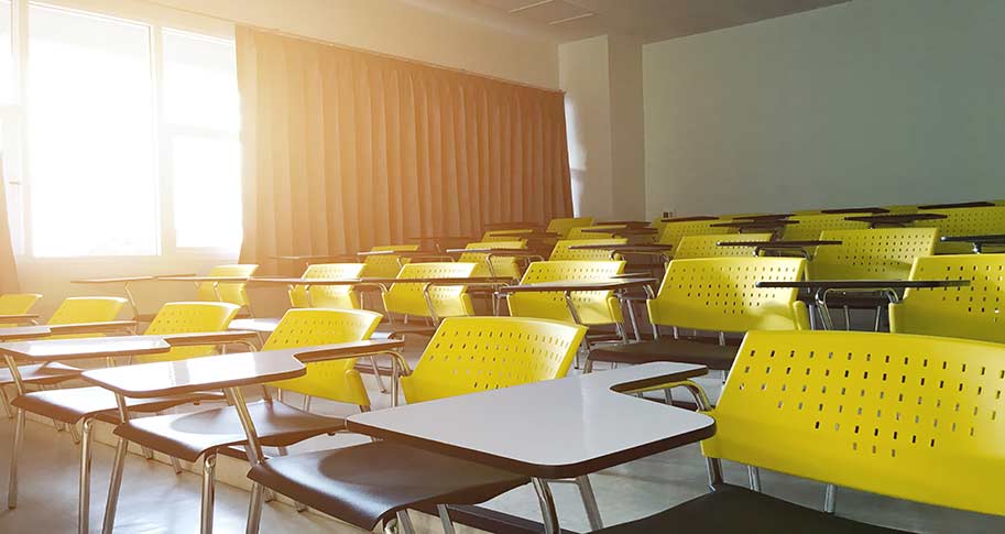 classroom of empty yellow and grey desks with bright summer sun in top left