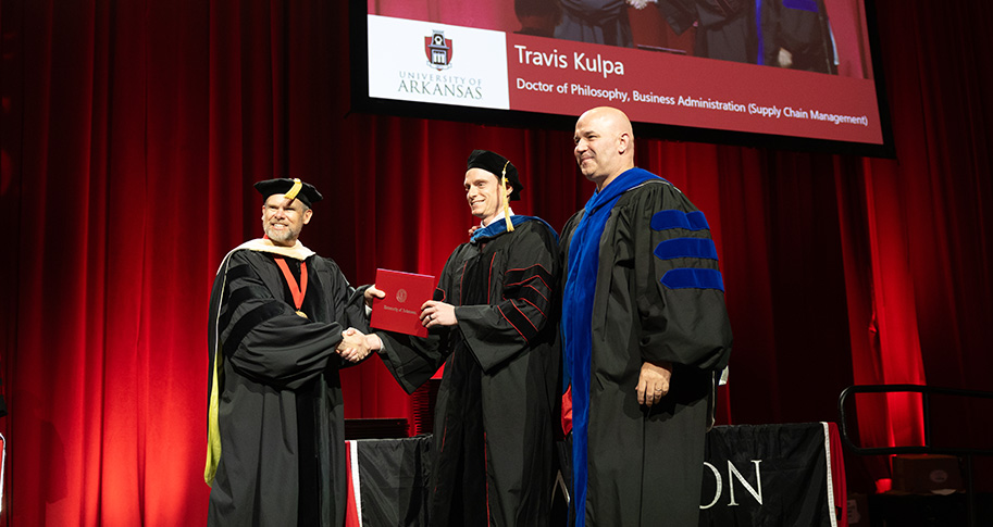 Dr. Gary Peters (far left), senior associate dean for the Sam M. Walton College of Business, and Dr. Rod Thomas (far right), faculty advisor, award Travis Kulpa a Doctor of Philosophy in Business Administration with a concentration in supply chain management in May.