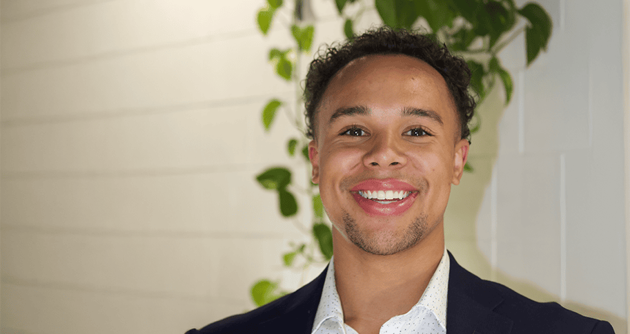 A student, Kendall Jasper posing for a headshot with a plant behind his head.