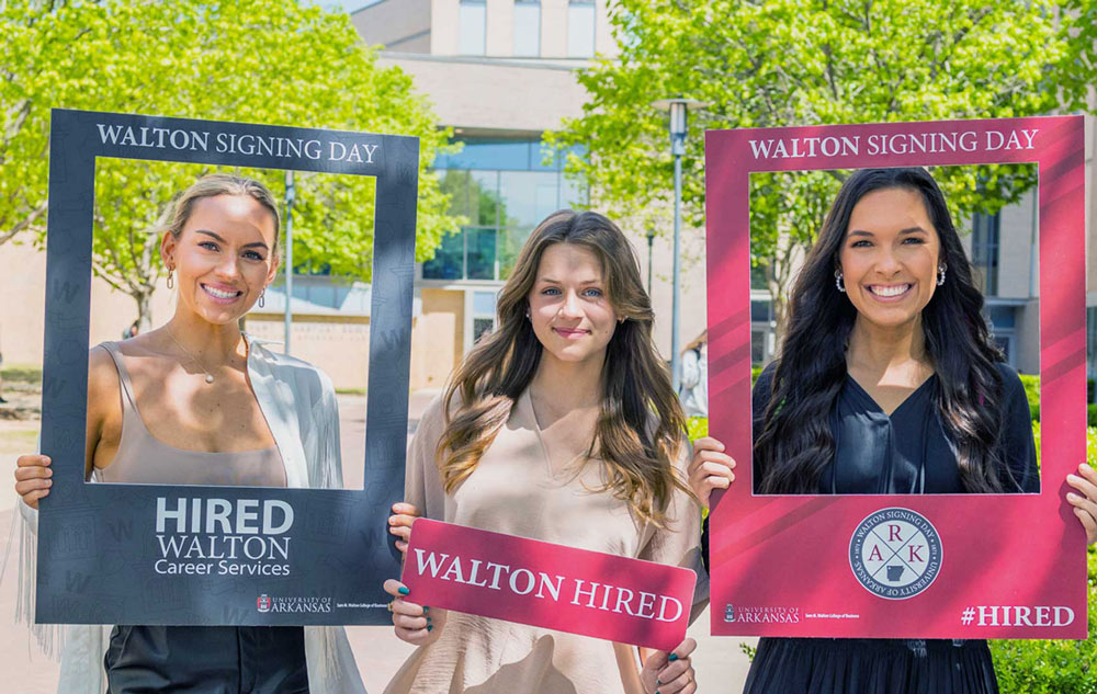 Three Walton College students holding 'Walton Hired' signs.